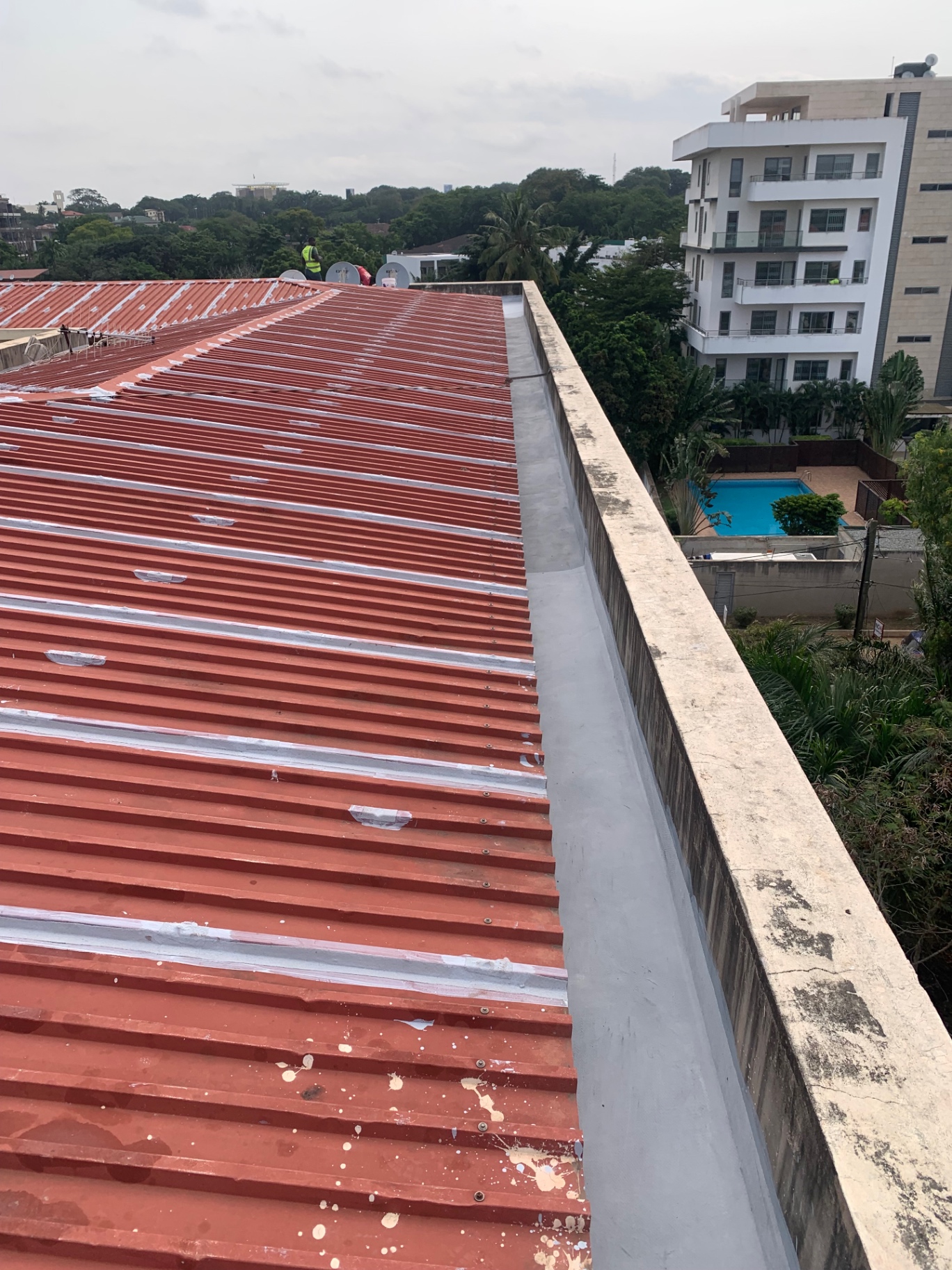 Red metal roof seam sealing alongside concrete parapet wall
