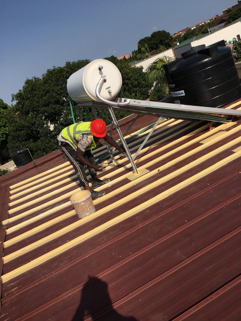 Technician applying primer coat under solar water heater on metal roof
